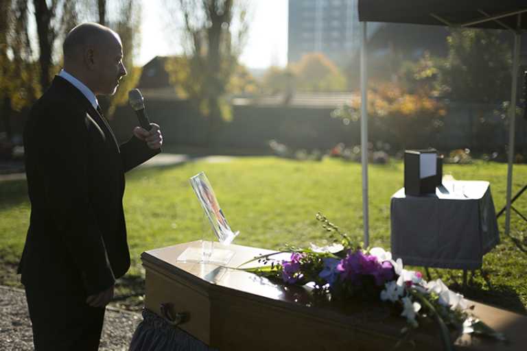 Maître de cérémonie devant un cercueil fleuri au cimetière, discours aux proches